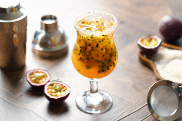 Tasty passion fruit drink in glass, fresh fruits, shaker and strainer on wooden table, closeup