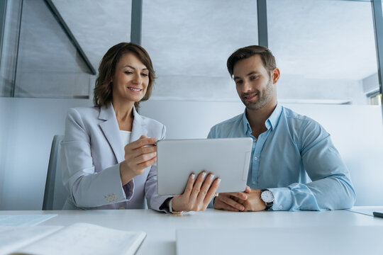 Two colleagues, group of partners, businessman and business woman working on pc gadget, closeup. Mature Latin businesswoman mentoring young European man discussing project on tablet device in office.