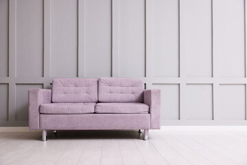 Comfortable violet sofa near gray wall in room