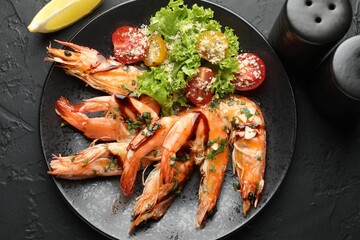 Tasty grilled shrimps served with salad and lemon on black table, flat lay. Delicious seafood dish