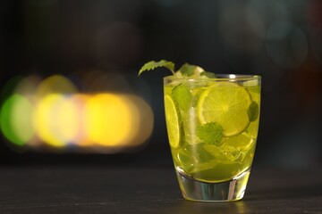 Glass of alcoholic cocktail with lime slices on table against blurred background. Space for text