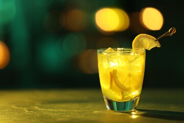 Glass of alcoholic cocktail with lemon slices on table against blurred background. Space for text