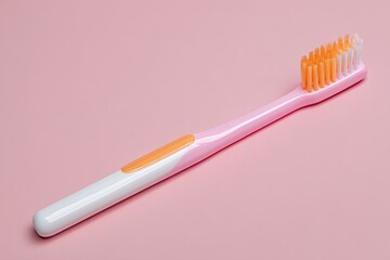 Pink toothbrush lying on a pink surface.  The toothbrush is plastic with a pink handle, white accents, and orange bristles