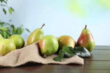 Fresh ripe pears on wooden table and green leaves outdoors, closeup