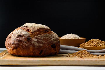 Freshly baked sourdough bread placed on a brown wooden cutting board with wheat flour on a black background