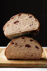 Freshly baked sourdough bread sliced ​​in half on a brown wooden cutting board on a black background