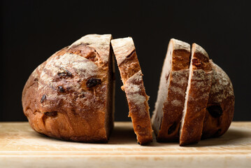 Freshly baked sourdough bread sliced ​​on a brown wooden cutting board on a black background