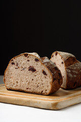 Freshly baked sourdough bread sliced ​​in half on a brown wooden cutting board on a black background