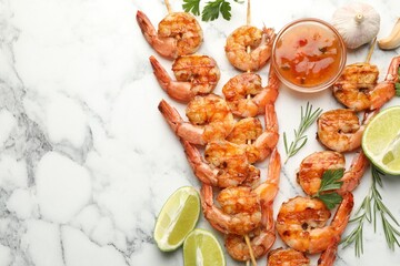 Skewers with tasty grilled shrimps, lime slices, herbs and sauce on white marble table, flat lay with space for text. Delicious seafood dish
