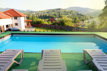 Obraz premium Empty sun loungers on artificial grass near outdoor swimming pool