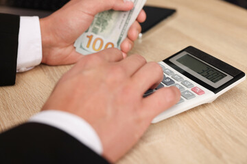 Man counting dollar banknotes at wooden table, closeup