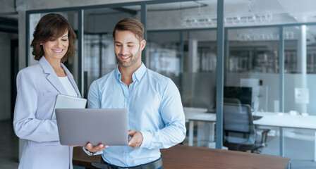 Banner with copy space of team of partners mature Latin businesswoman, young business man discussing project on laptop in office. Two professional people mentor teacher and intern working together