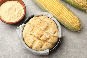 Freshly baked cornbread in cake pan, cobs and flour on grey textured table, flat lay