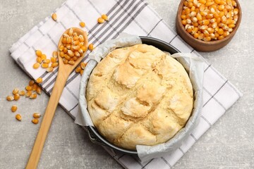 Freshly baked cornbread in cake pan, seeds and spoon on grey textured table, flat lay