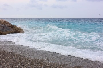 Beautiful view of wavy sea, rocks and pebbles on beach