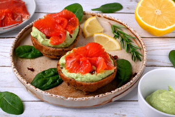 Bruschetta with smoked trout fish and avocado cream on bread served on the ceramic plate with lemon and herbs