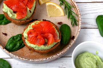 Bruschetta with smoked trout fish and avocado cream on bread served on the ceramic plate with lemon and herbs