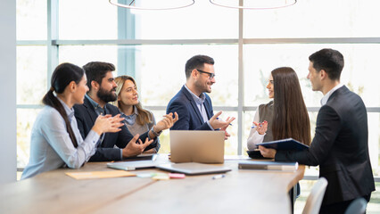 Businessman is proposing promotion for young female colleague and is congratulating her in front of team