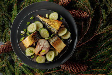 Smoked mackerel with fresh cucumber and green onions on a black plate.