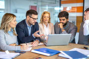Business people are sitting around table in front of laptop carefully observing work while creating strategy