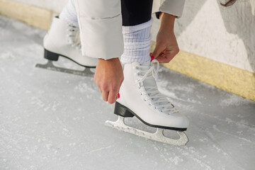 Tying white figure skates on ice rink. Seasonal fun