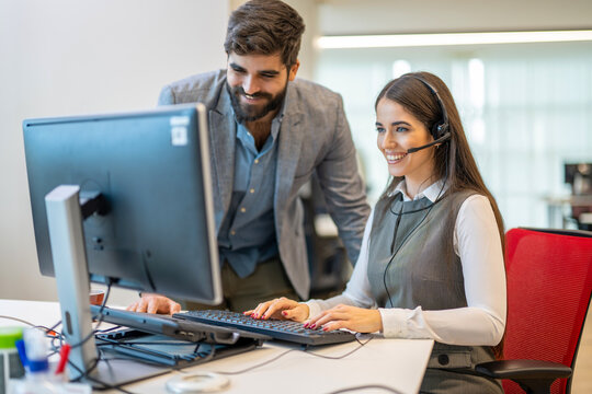 Business man is standing next to female colleague representing call center agent while assisting with data on computer