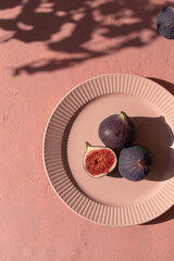 Plate with ripe figs fruit on the mediterranean pink terracotta color plaster background with leaves shadows.	