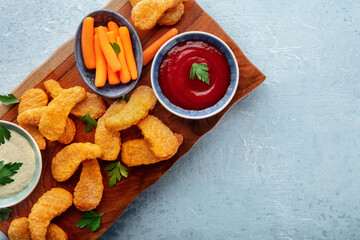 Chicken nuggets with fresh vegetables and dips, on a wooden board, overhead flat lay shot with copy space
