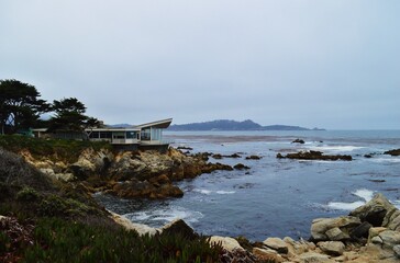 Modern house on a rocky cliff overlooking the Pacific Ocean in Carmel, California, with coastal landscape and ocean waves