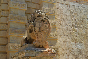 Stone lion sculpture holding a coat of arms at the entrance gate of Mdina, Malta, symbol of heritage and medieval architecture