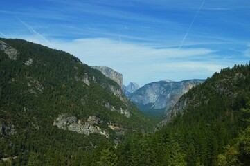 Scenic view of El Capitan and Half Dome in Yosemite National Park, California, with forested mountains under a clear blue sky