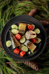 Smoked mackerel with fresh cucumbers, tomatoes and green onions on a black plate.