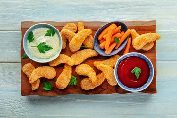 Chicken nuggets with fresh vegetables and dips, overhead flat lay shot on a wooden table, with parsley