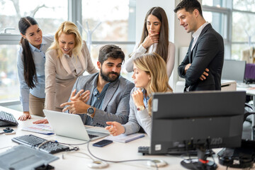 Group of business people gathered around boss with laptop discussing positive business decisions and company development