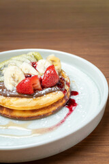 Stacked pancakes presenting chocolate spread, fresh kiwi, banana, and strawberry on a plate
