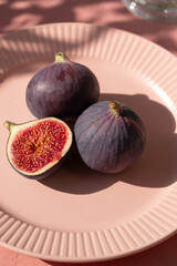Plate with ripe figs fruit on the mediterranean pink terracotta color plaster background with leaves shadows.