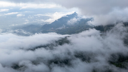 Aerial of Village in rain cloud cover tropical green mountain. Rainy season. Misty cover green forest. beautiful green village
