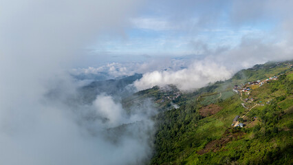 Aerial of Village in rain cloud cover tropical green mountain. Rainy season. Misty cover green forest. beautiful green village