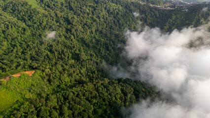 Aerial of Village in rain cloud cover tropical green mountain. Rainy season. Misty cover green...