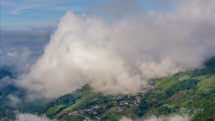 Aerial of Village in rain cloud cover tropical green mountain. Rainy season. Misty cover green forest. beautiful green village