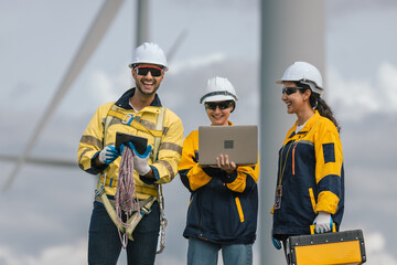 Group of multicultural engineers in safety gear working together at a wind farm, using digital devices to inspect renewable energy systems, promoting teamwork, innovation, and sustainable development.
