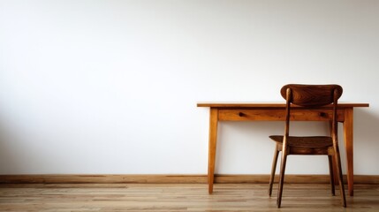 A simple desk with a chair placed near it against a plain neutral wall,