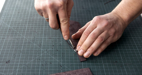Craftsman using edge tool on leather strip for handmade leather goods production