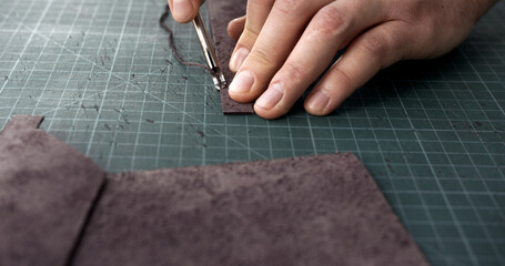 Craftsman using edge tool on leather strip for handmade leather goods production