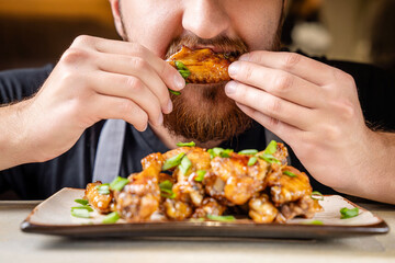 Man eating glazed chicken wings close-up