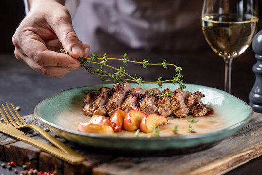 Chef plating gourmet duck breast with herbs