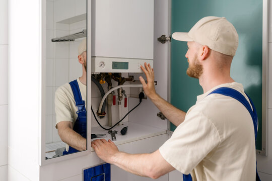 Repairman maintaining gas boiler in modern bathroom for efficient heating