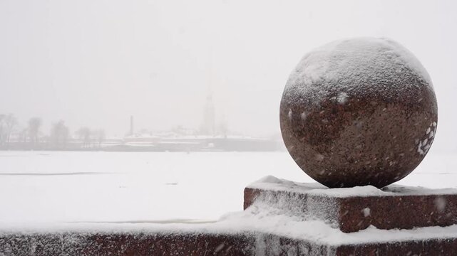 Granite ball on the embankment of Strelka Vasilievsky island against the background of the Neva river in winter snowing