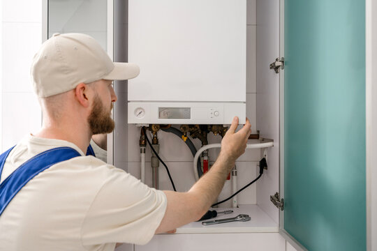 Repairman performs maintenance on gas boiler in modern bathroom space
