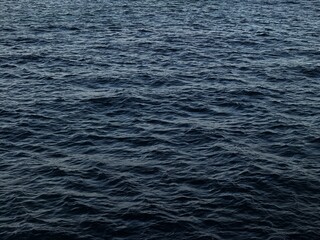 Small waves in the dark mediterranean sea, the evening light creates contrast and reflection with different gradients of blue from light to ultramarine blue.